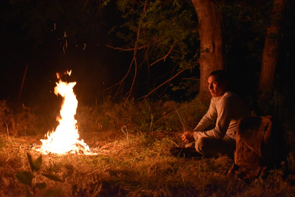 Zachary Hokeah sitzt am Lagerfeuer in Consume.